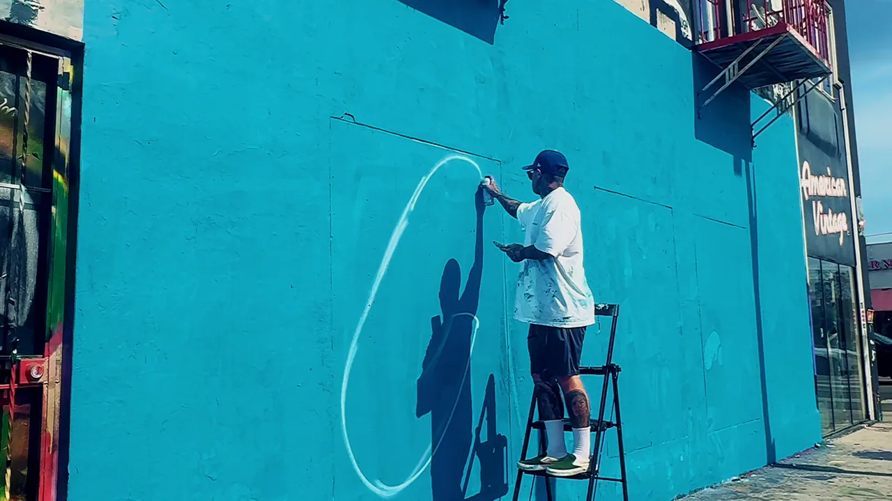 An artist painting the blue Cookies mural on Melrose